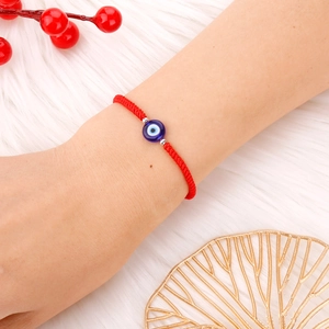 Detail of red woven Evil Eye bracelet with blue bead on a white plush background