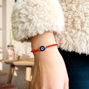 Handmade red braided Evil Eye bracelet for protection worn on wrist with cozy background