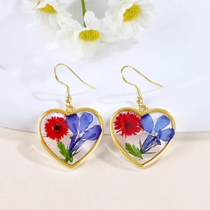 Detail of heart-shaped gold resin earrings with dried red and blue flowers and green leaves