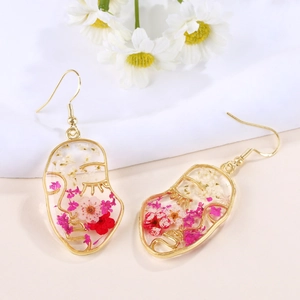 Close-up of gold face earrings with resin and real dried flowers in red and pink