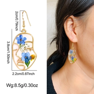 Detail shot of irregular gold face earrings with real dried flowers and dimensions
