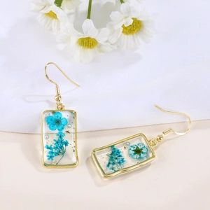 Detail of rectangular gold earrings featuring real blue dried flowers and gold leaf foil