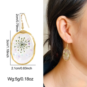 Macro detail of oval earrings with real dried flowers and rainbow resin in gold frames