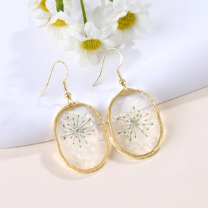 Detail view of handmade gold earrings featuring real dried flowers in irregular resin charms