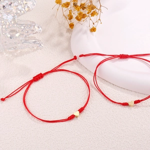 Macro view of adjustable red braided rope bracelet with gold heart charm on white ceramic