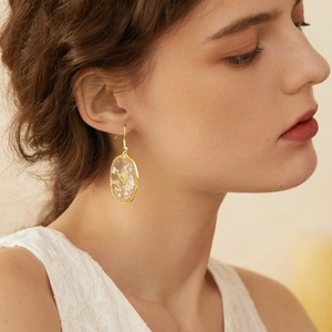 Detailed view of handmade gold drop earrings featuring white dried flowers in clear resin