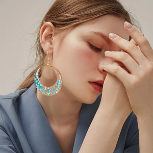 Detail view of model wearing gold resin hoop earrings with blue dried flowers