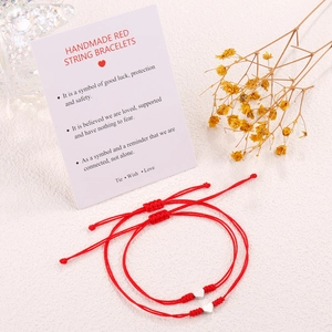 Detail of red braided lucky knot bracelets with silver heart charms on card