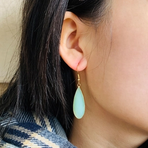 Élégantes boucles d'oreilles goutte d'or avec pierre vert clair portées par un mannequin