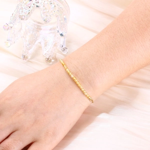 Detail of 3mm gold-plated beaded bracelet worn on wrist against silk fabric