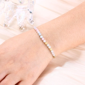 Close-up of a colorful beaded bracelet with gold metal accents on a pink silk background