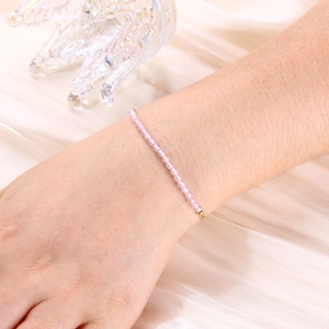 Close-up of a pink beaded bracelet with gold clasp on silk background worn on a wrist