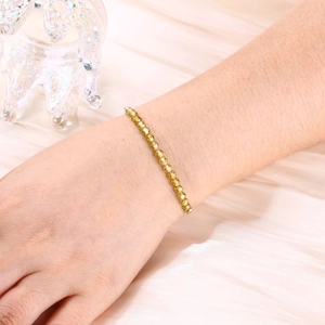 Detail of 4mm gold beaded bracelet with faceted beads worn on wrist with silk background
