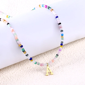 Dettaglio della collana di perline colorate con pendente lettera A dorata su supporto bianco