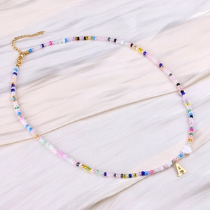 Close-up of colorful seed bead necklace with a gold letter A pendant and white heart bead