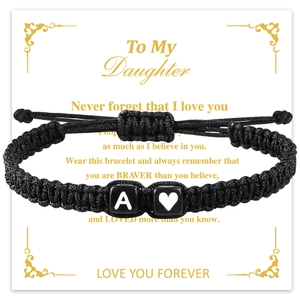 Detalle de pulsera de cordón trenzado negro con cuentas de A y corazón en tarjeta