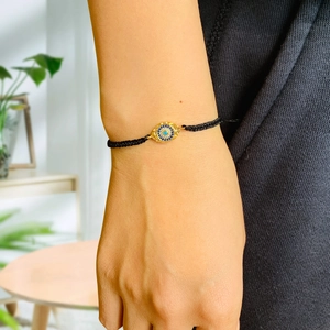 Detailed view of adjustable black braided bracelet with golden Evil Eye charm