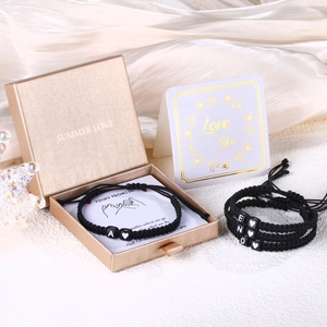 Detalle de pulseras de promesa tejidas con cuentas de letras en caja de regalo dorada