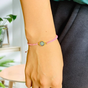 Detailed shot of pink woven Evil Eye bracelet with gold-plated charm on model wrist