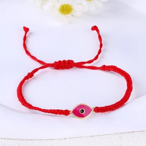 Detail of red hand-woven evil eye bracelet with pink pendant on a white fabric background