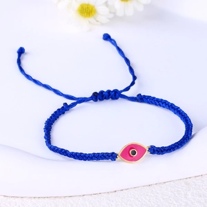 Detailed view of hand-woven blue cord bracelet with pink evil eye charm on a white tray