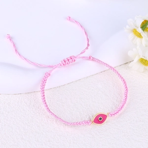 Macro detail of pink hand-woven rope bracelet featuring a gold evil eye charm