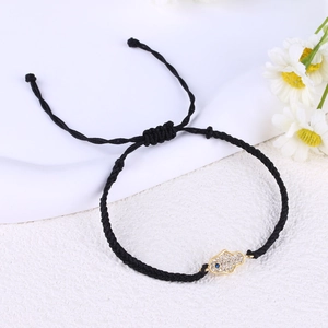 Close-up of black braided bracelet with gold Hamsa hand charm and blue eye zircon