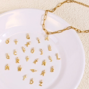 Pendentifs alphabet dorés avec zircons sur collier trombone posé sur plateau blanc