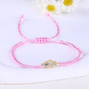Macro detail of a pink braided Hamsa Hand bracelet with gold and blue zircon accents