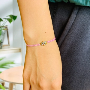 Detailed close-up of pink braided bracelet featuring a colorful gemstone Hamsa hand charm