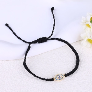 Macro detail of hand-woven black cord bracelet with golden evil eye zircon pendant