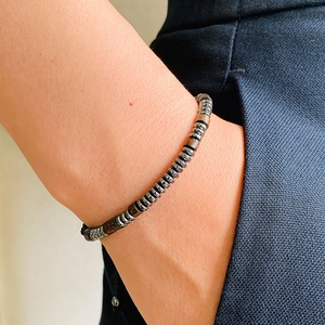 Close-up of Morse code braided bracelet with hematite beads and wooden texture on wrist