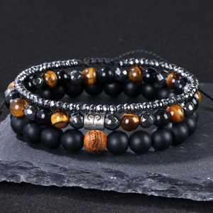 Nahaufnahme von Tigerauge- und Onyx-Armbändern mit Widder-Symbol auf Schieferbasis