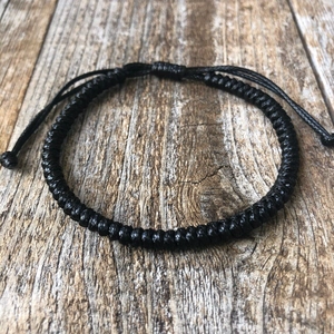 Detail of the thick black handmade braided rope bracelet on a rustic wood background