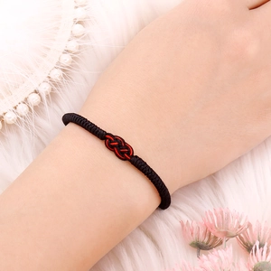 Detailed view of a thick black braided knot bracelet with a red accent on plush background