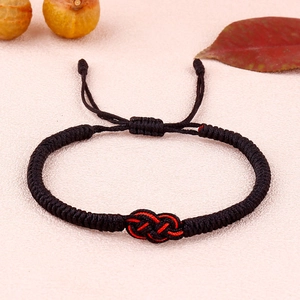 Close-up of handmade Tibetan knot bracelet featuring thick black braided cord with red accents