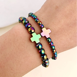 Dettaglio di braccialetti con perline arcobaleno metalliche e ciondoli a croce