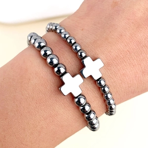 Dettaglio di bracciali in ematite scura lucida con ciondoli a croce in metallo da uomo