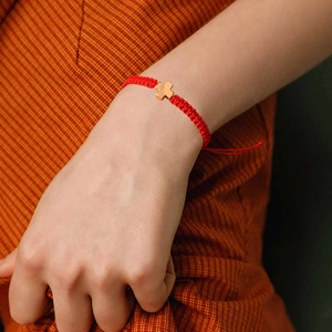 Detail eines handgefertigten roten geflochtenen Armbands mit goldenem Kreuzanhänger