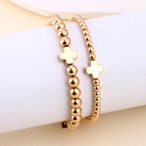 Dettaglio di doppi bracciali elastici con perline dorate e ciondoli a croce in metallo