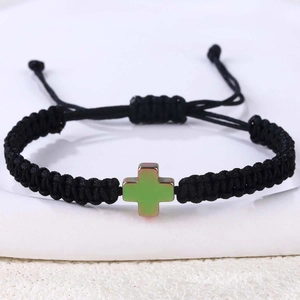 Detailaufnahme eines handgewebten schwarzen Armbands mit einem grünem Kreuzanhänger