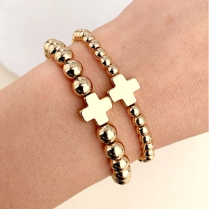 Primo piano dettagliato di bracciali elastici con perline dorate e ciondoli a croce