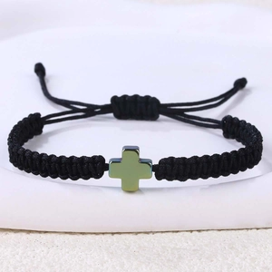 Detail eines verstellbaren schwarzen geflochtenen Armbands mit grünem Kreuzanhänger