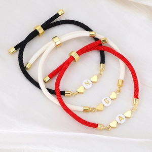 Macro detail of braided heart bracelets with initial beads on white silk backdrop