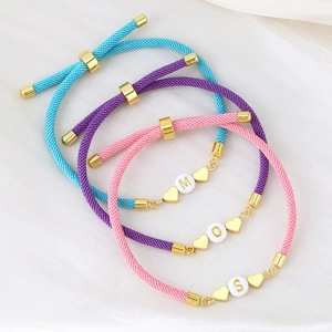 Close-up of woven couple bracelets with gold letter beads and heart charms on silk