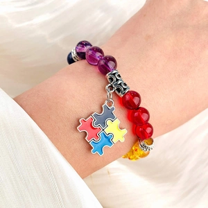 Detail of colorful beaded bracelet with a four-color enamel puzzle piece charm on wrist