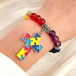 Close-up of a colorful beaded bracelet with a puzzle-patterned cross charm on a wrist