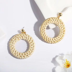 Close-up of handmade woven rattan hoop earrings with gold sphere studs in boho style