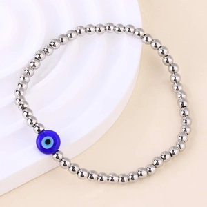 Detail van zilveren kralenarmband met blauw boze oog op een wit voetstuk