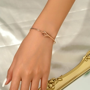 Vista dettagliata di un bracciale a nodo in oro rosa indossato al polso su seta bianca